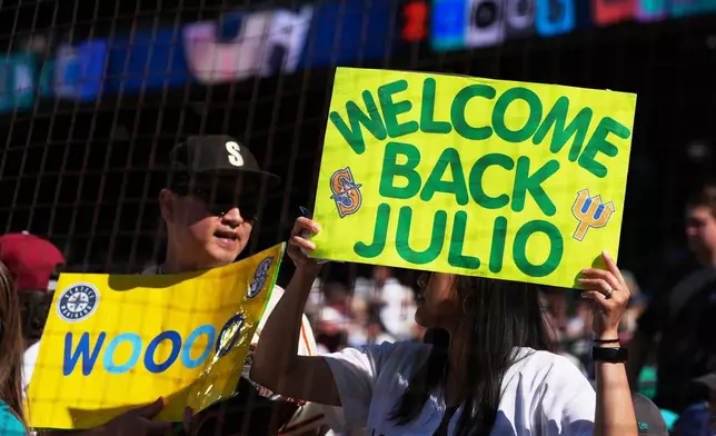 Fans hold signs for Seattle Mariners designated hitter Julio Rodríguez before a baseball game between the Seattle Mariners and the San Francisco Giants, Saturday, July 18, 2026, in Seattle. (AP Photo/Lindsey Wasson)