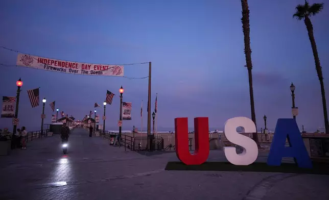 A person rides a scooter past a large "USA" installation on Independence Day in Huntington Beach, Calif., Saturday, July 4, 2026. (AP Photo/Jae C. Hong)