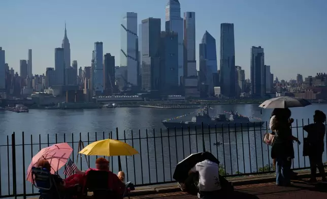 People take cover from the heat under umbrellas as they wait for a parade of tall ships and flyovers in Weehawken, N.J., Saturday, July 4, 2026. (AP Photo/Seth Wenig)