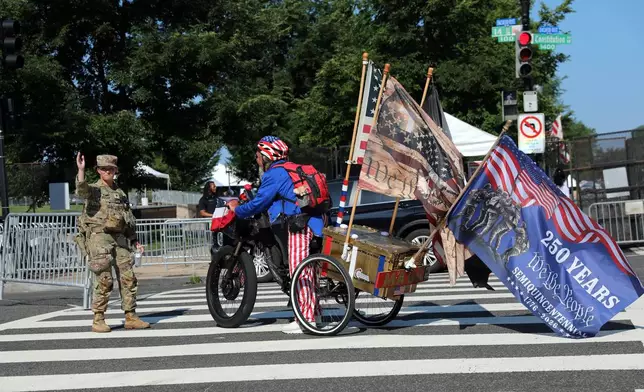 Members of the National Guard direct a person riding a bicycle with various flags attached to a cart before an Independence Day event honoring the nation's 250th anniversary, Saturday, July 4, 2026, on the National Mall in Washington. (AP Photo/Rahmat Gul)