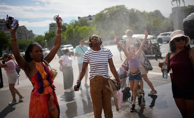 Tourists enjoy cooling off at a public water fountain In Paris, Friday, June 26, 2026. (AP Photo/Christophe Ena )