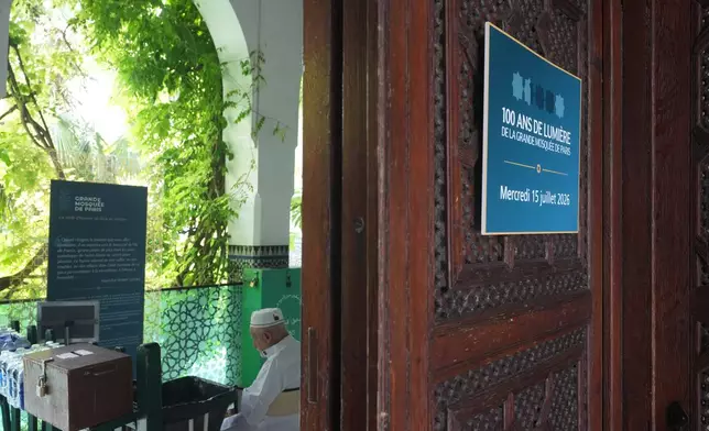 A man sits at the entrance of Paris' Grand Mosque where a blacard reads "100 Years of Light" marking its centenary, Friday, July 17, 2026. (AP Photo/Michel Euler)