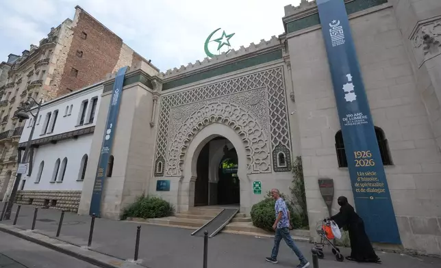 People walk past the Grand Mosque of Paris, where a banner reads, "100 years of light, a century of history, spirituality and dialogue" marking its 100th anniversary, Friday, July 17, 2026. (AP Photo/Michel Euler)