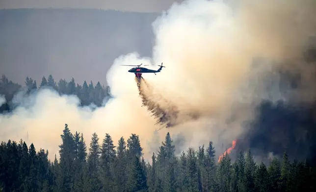 A helicopter drops water on the Akawa Butte fire on Friday, July 24, 2026, near Sisters, Ore. (AP Photo/Noah Berger)