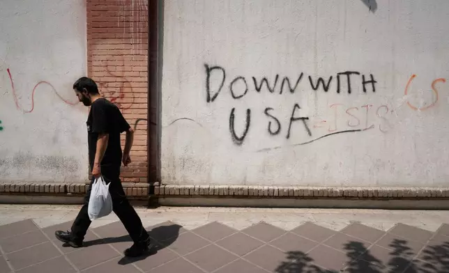 A man walks past anti-U.S. graffiti on the wall of the British Embassy in Tehran, Iran, Monday, July 27, 2026. (AP Photo/Vahid Salemi)
