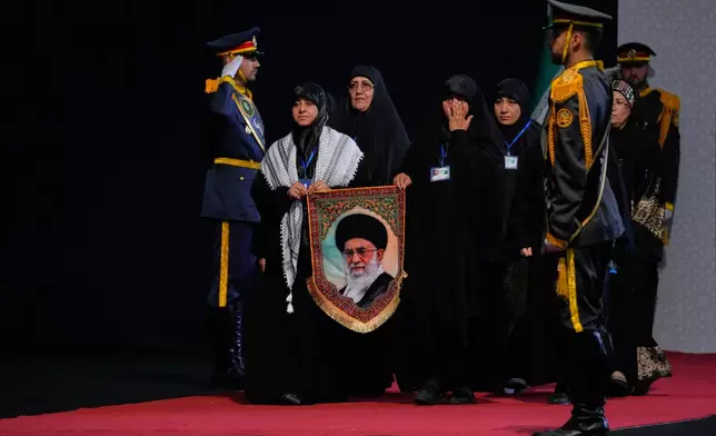 Women carry a portrait of slain Iranian Supreme Leader Ayatollah Ali Khamenei as they arrive to pay their respects before the coffins of Khamenei and members of his family during a viewing ceremony ahead of the dayslong funeral ceremonies at the Imam Khomeini Mosalla Grand Mosque in Tehran, Iran, Friday, July 3, 2026. (AP Photo/Vahid Salemi)