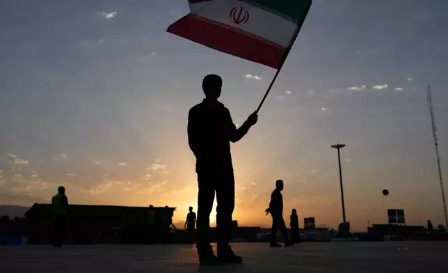 The sun rises as a man holds an Iranian flag on the esplanade of the Imam Khomeini Mosalla Grand Mosque before the start of the dayslong funeral ceremonies for slain Iranian Supreme Leader Ayatollah Ali Khamenei and members of his family in Tehran, Iran, Saturday, July 4, 2026. (AP Photo/Altaf Qadri)