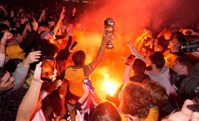 Fans gather around a burning flare as the prepare to watch large screens in a park in Sydney, Saturday, July 4, 2026, as Australia and Egypt play in their World Cup round of 32 soccer match. (AP Photo/Rick Rycroft)