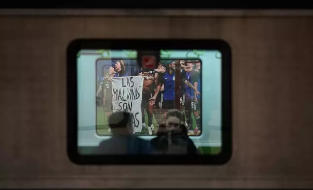 People ride a subway train stopped at a station displaying a photo of Argentina's soccer players holding a banner reading "The Malvinas are Argentine," referring to the Falkland Islands also known as Malvinas, taken after the team's World Cup semifinal soccer match between Argentina and England, in Buenos Aires, Argentina, Monday, July 27, 2026. (AP Photo/Natacha Pisarenko)