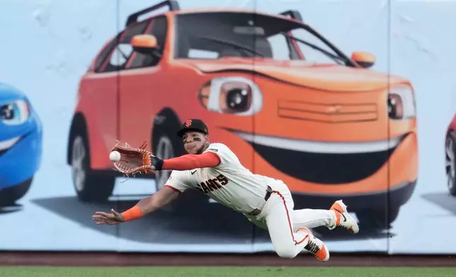 San Francisco Giants left fielder Victor Bericoto dives to catch a fly out hit by Colorado Rockies' Cole Carrigg during the first inning of a baseball game Thursday, July 9, 2026, in San Francisco. (AP Photo/Jeff Chiu)