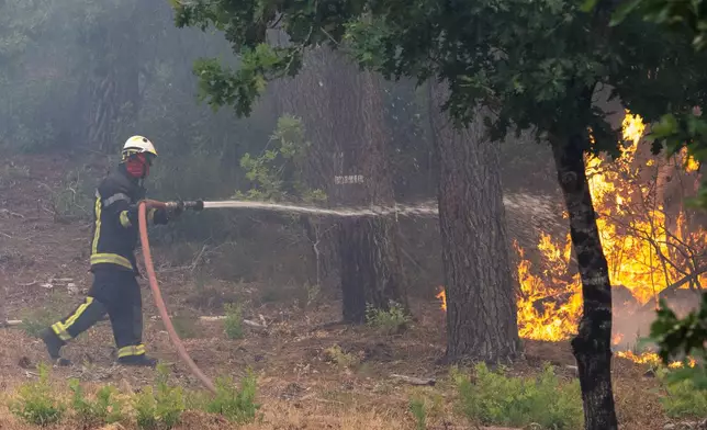 A firefighter sprays water in a burning forest in the Lège-Cap-Ferret region, western France, Friday, July 24, 2026. (AP Photo/Caroline Blumberg)