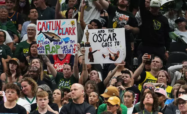 Fans wave signs referencing Indiana Fever guard Caitlin Clark during the second half of a WNBA basketball game between the Seattle Storm and the Indiana Fever, Tuesday, July 28, 2026, in Seattle. (AP Photo/Lindsey Wasson)