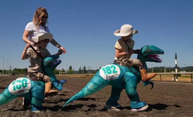 Young racers walk on the track to the starting gate for a kids' heat during the T-Rex World Championship Races at Emerald Downs, Sunday, July 12, 2026, in Auburn, Wash. (AP Photo/Lindsey Wasson)