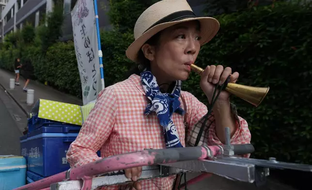 Akiko Sugaya blows an old-style horn while she peddles tofu, prepared food and beverages in a cart in Tokyo, Saturday, July 4, 2026. (AP Photo/Hiro Komae)