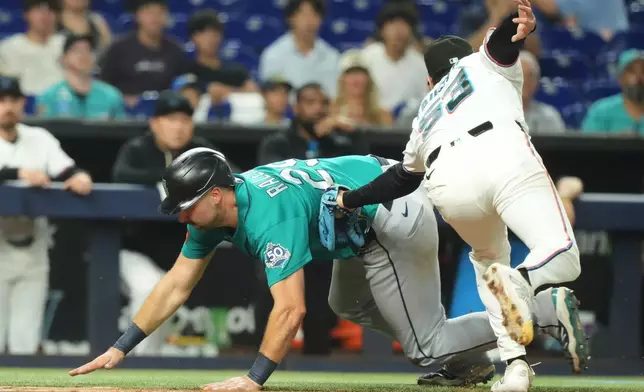 Miami Marlins relief pitcher Calvin Faucher (53 ) tags out Seattle Mariners' Cal Raleigh during the eighth inning of a baseball game Tuesday, July 7, 2026, in Miami. (AP Photo/Marta Lavandier)