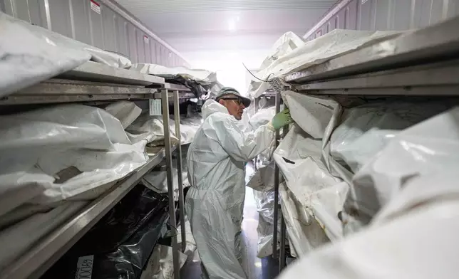 A morgue worker searches for a body of Ukrainian soldier before examination at the forensic bureau in Kyiv region, Ukraine, on Monday, June 1, 2026. (AP Photo/Evgeniy Maloletka)