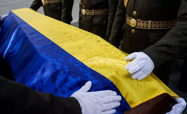 An honor guard straightens out the flag draped over the coffin of a unidentified Ukrainian soldier killed in battle during the Russian-Ukrainian war, during a funeral ceremony at a military cemetery near Kyiv, Ukraine, Thursday, April 30, 2026. (AP Photo/Evgeniy Maloletka)