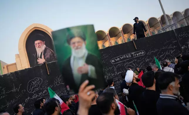 A mourner holds a portrait of the late Iranian Supreme Leader Ayatollah Ali Khamenei as he walks past a wall bearing messages, including one in English that reads "We will kill Trump," during the funeral ceremonies for Khamenei and members of his family at the Imam Khomeini Mosalla Grand Mosque in Tehran, Iran, Saturday, July 4, 2026. (AP Photo/Altaf Qadri)