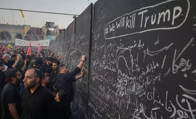 Mourners write messages on a wall, including one in English that reads "We will kill Trump," during the funeral ceremonies for slain Iranian Supreme Leader Ayatollah Ali Khamenei and members of his family at the Imam Khomeini Mosalla Grand Mosque in Tehran, Iran, Saturday, July 4, 2026. (AP Photo/Altaf Qadri)