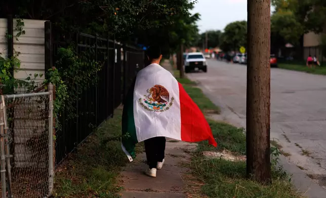 A man walks home draped in a Mexican flag after a vigil for Lorenzo Salgado Araujo, a Mexican national fatally shot by a federal immigration agent a day prior, Wednesday, July 8, 2026, in Houston. (AP Photo/Mark Felix)