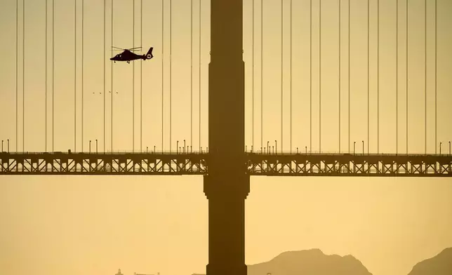 A helicopter flies past the Golden Gate Bridge while searching for missing victims after a boat accident near Alcatraz Island off San Francisco, Tuesday, July 14, 2026. (AP Photo/Noah Berger)