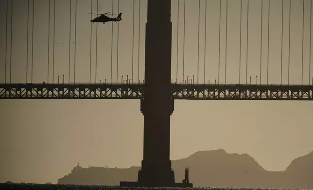 A helicopter goes past the Golden Gate Bridge as part of search and rescue efforts near the site of boat accident on Tuesday, July 14, 2026, in San Francisco. (AP Photo/Noah Berger)
