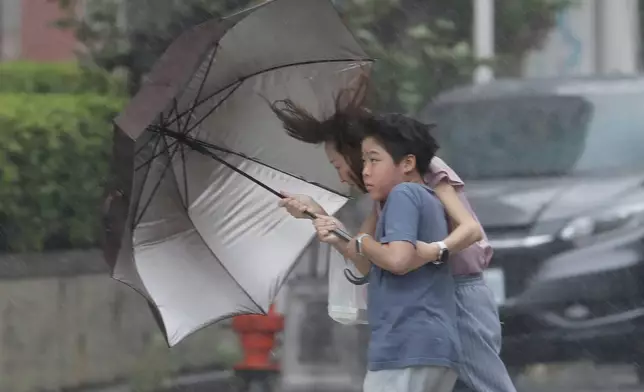 People struggle with umbrella in a rain caused by Typhoon Bavi in Taichung, Taiwan, Saturday, July 11, 2026. (AP Photo/Chiang Ying-ying)