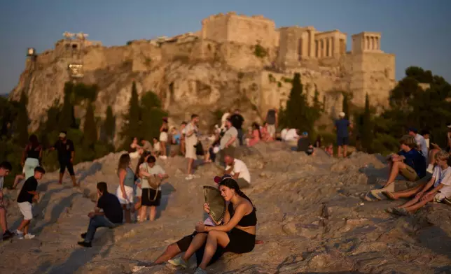 A tourist uses a hand fan to cool off during a heat wave as people gather on Areopagus Hill, with the Acropolis in the background, in Athens, Tuesday, July 21, 2026. (AP Photo/Petros Giannakouris)