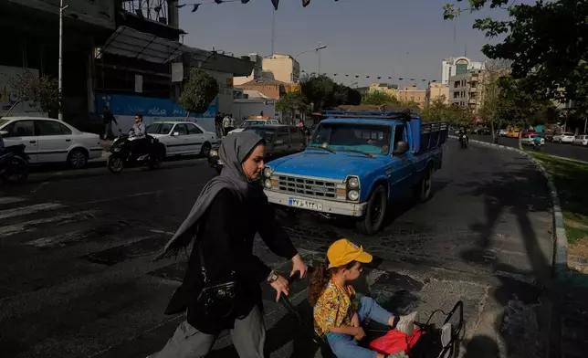 A woman crosses a street with a girl in downtown Tehran, Iran, Wednesday, July 22, 2026. (AP Photo/Vahid Salemi)