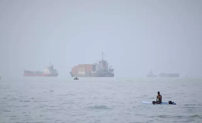 FILE - A man sits on a surfboard as a container ship and other commercial vessels appear anchored in the Strait of Hormuz off Bandar Abbas, Iran, Monday, July 27, 2026. (Razieh Poudat/ISNA via AP, File)