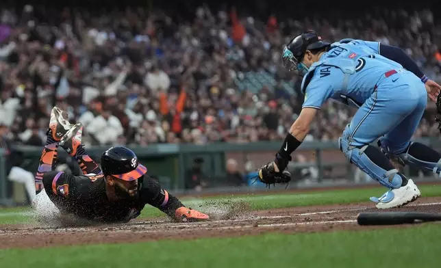 San Francisco Giants' Heliot Ramos, left, slides home to score against Toronto Blue Jays catcher Brandon Valenzuela during the fifth inning of a baseball game Tuesday, July 7, 2026, in San Francisco. (AP Photo/Jeff Chiu)