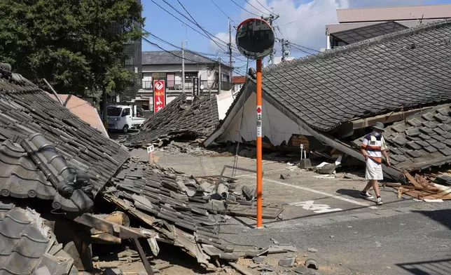 A person walks past the houses collapsed in an earthquake in Yatsushiro, Kumamoto Prefecture, southern Japan, Friday, July 31, 2026. (Koji Harada/Kyodo News via AP)