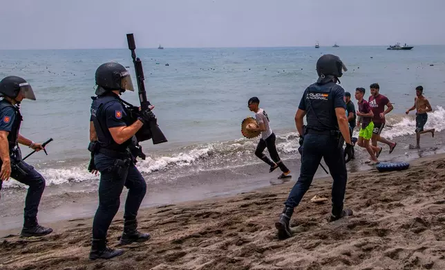 Spanish police officers respond as migrants cross from Morocco into the Spanish enclave of Ceuta, Thursday, July 30, 2026. (AP Photo/Antonio Sempere)
