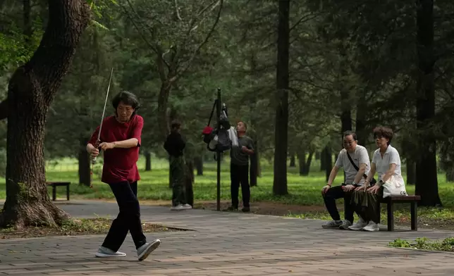 A couple watch a woman practice Tai Chi with a sword at a park near the Temple of Heaven in Beijing, Thursday July 9, 2026. (AP Photo/Andy Wong)