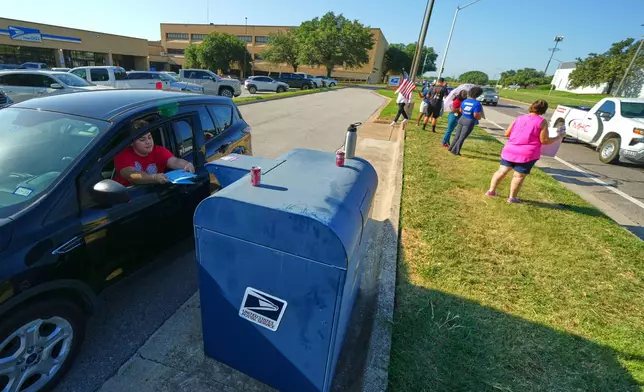 A person drops envelopes into a mailbox as postal workers participate in a national day of action outside a U.S. Post Office building, Tuesday, July 28, 2026, in Fort Worth, Texas. (AP Photo/Julio Cortez)