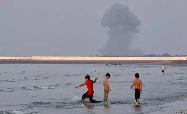 Three boys play in the shallow waters of the Strait of Hormuz, as a plume of smoke rises from an explosion in the background, off Bandar Abbas, Iran, Monday, July 13, 2026. (Razieh Poudat/ISNA via AP)