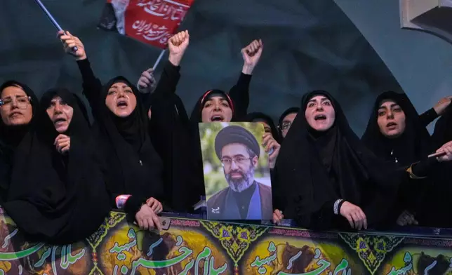 Mourners chant slogan as one of them holds a poster of the Supreme Leader Ayatollah Mojtaba Khamenei in a ceremony commemorating the late Supreme Leader Ayatollah Ali Khamenei at the Imam Khomeini Mosalla Grand Mosque in Tehran, Tuesday, July 14, 2026. (AP Photo/Vahid Salemi)