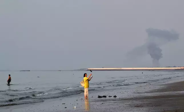 A woman stands at the water's edge along the Strait of Hormuz as a plume of smoke rises in the background following an explosion, off Bandar Abbas, Iran, Monday, July 13, 2026. (Razieh Poudat/ISNA via AP)