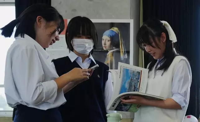 Chiho Ninomiya, from left, Kanami Murata and Karin Makishima, freshman members of the art club at Kumagaya Girls High School, discuss ideas for chalk art drawing at the school in Kumagaya, northwest of Tokyo, Tuesday, July 21, 2026, as they are part of the team participating in a national blackboard art contest. (AP Photo/Hiro Komae)