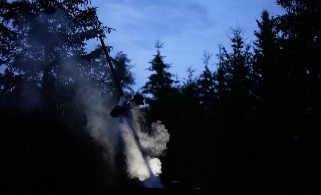 Immo Feldmer uses a pole as he stands on a mound of earth at his family-run, traditional charcoal production site near Hasselfelde in Germany's Harz forest, late Monday, July 6, 2026. (AP Photo/Matthias Schrader)