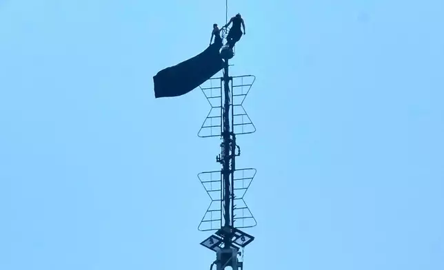 Two people stand on the tip of the antenna of the Empire State Building while holding a banner on Wednesday, July 1, 2026. (AP Photo/Richard Drew)