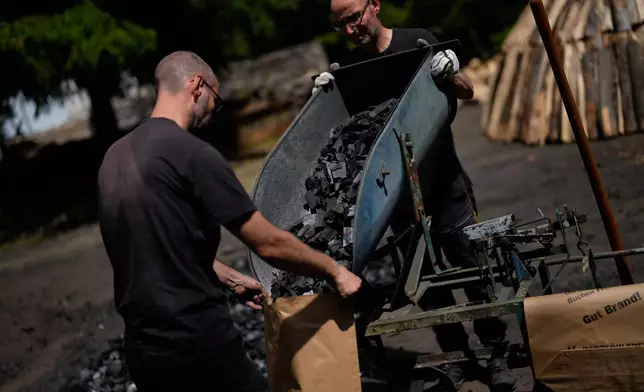 Brothers Immo and Sascha Feldmer put charcoal into paper bags after weighing it at their traditional production site near Hasselfelde in Germany's Harz, Germany, Thursday, June 18, 2026. (AP Photo/Matthias Schrader)