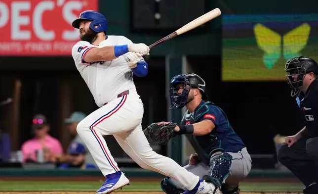 Texas Rangers' Jake Burger follows through on a two-run home run as Seattle Mariners catcher Mitch Garver and umpire Derek Thomas look on in the third inning of a baseball game in Arlington, Texas, Monday, July 27, 2026. (AP Photo/Tony Gutierrez)