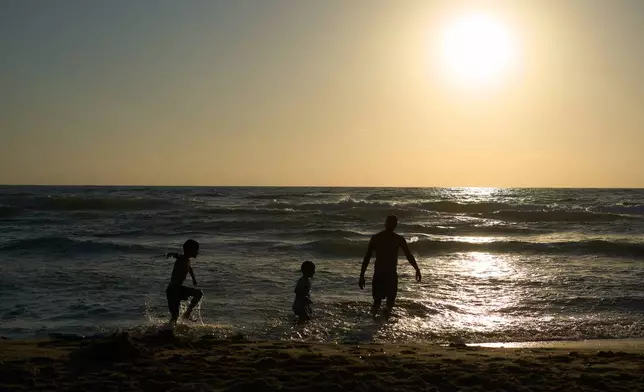 A family enjoys part of the Mediterranean Sea that is near a military firing range that is slated to be cleared in Rishon LeZion on Tuesday, June 23, 2026. (AP Photo/Ariel Schalit)