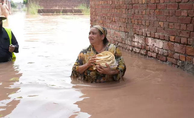 A woman heads back to his home after receiving food for her family provided by rescue workers at a flooded area near Lahore, Pakistan, Monday, Jun 27, 2026. (AP Photo/K.M. Chaudary)