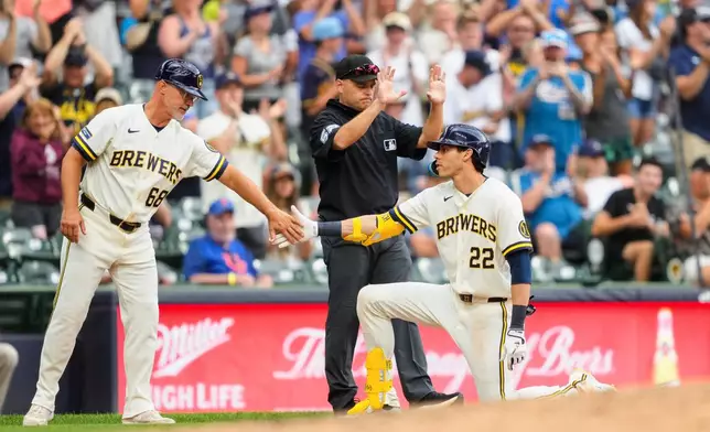 Milwaukee Brewers designated hitter Christian Yelich (22) high-fives third base coach Matt Erickson (68) after hitting an RBI triple as umpire Jansen Visconti (52) looks on during the sixth inning of a baseball game against the New York Mets, Wednesday, July 22, 2026, in Milwaukee. (AP Photo/Kayla Wolf)