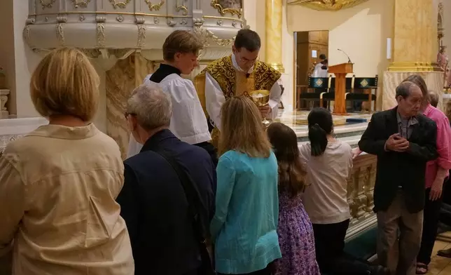 The faithful at the Church of Saint Agnes receive communion on the tongue and while kneeling at the altar rails, in the traditional custom, during one of the Catholic parish’s Latin Masses in St. Paul, Minn., Sunday, June 28, 2026. (AP Photo/Giovanna Dell’Orto)