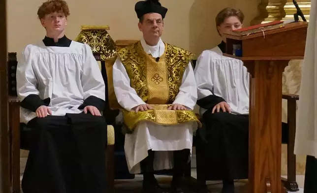 The Rev. John Ubel, pastor of the Church of Saint Agnes, wears the traditional biretta hat and vestments as he sits between altar servers during one of the Catholic parish’s Latin Masses in St. Paul, Minn., Sunday, June 28, 2026. (AP Photo/Giovanna Dell’Orto)