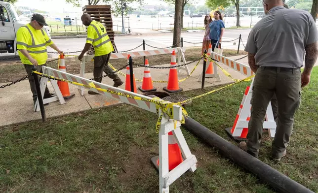 National Park Service workers adjust barricades around a manhole near the World War II Memorial next to the Lincoln Memorial Reflecting Pool, Friday, July 10, 2026, in Washington. (AP Photo/Mark Schiefelbein)
