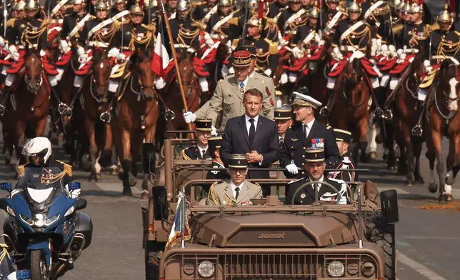 French President Emmanuel Macron, center, and General Chief of Staff of the French armed Forces Fabien Mandon stand in the command car as they review troops during the Bastille Day military parade on the Champs-Elysees avenue in Paris, Tuesday, July 14, 2026. (AP Photo/Thomas Padilla)